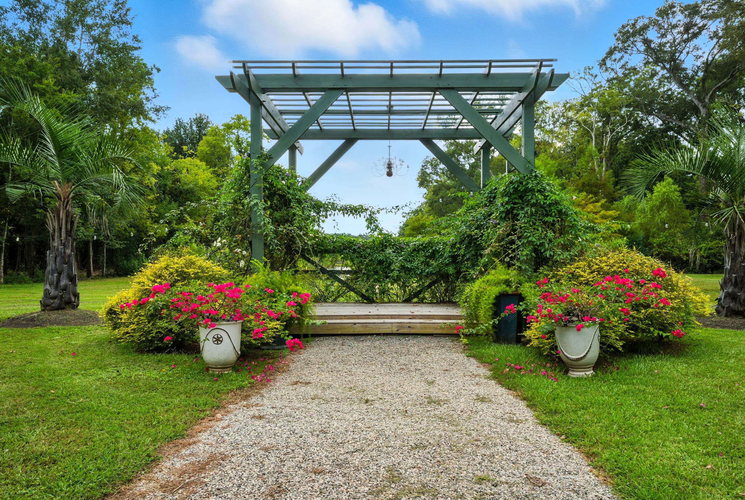 A gravel path leads to a green trellis adorned with lush vines and colorful flowers on either side.